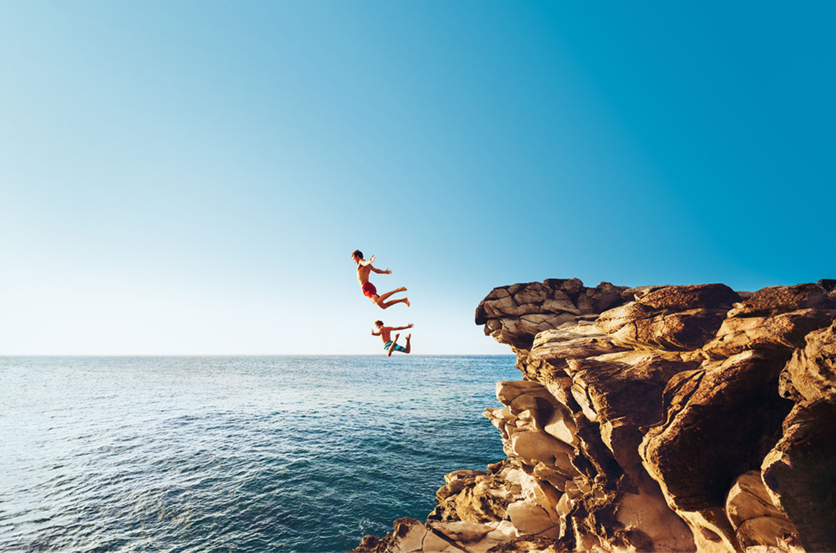 Zwei Männer springen von Klippe ins weite Meer, symbolisch für Bildbearbeitung - n c ag