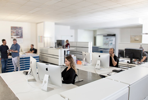 Verschiedene Mitarbeiter arbeiten am Computer und diskutieren im Büro, symbolisch für Corporate Publishing - n c ag